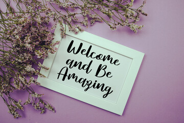 Welcome and Be Amazing text with flowers bouquet decoration on purple background