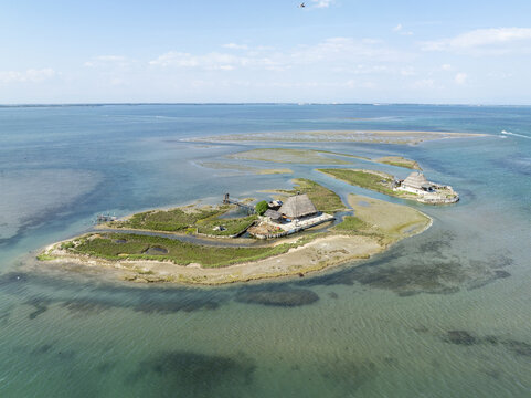 Aerial view of sun-kissed islands reveal the rustic charm of traditional thatched-roof buildings amidst the shimmering turquoise waters of the lagoon, Marano Lagunare, Friuli-Venezia Giulia, Italy.