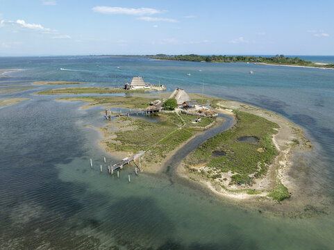 Aerial view of rustic thatched structures nestled on an island, encircled by the tranquil, turquoise waters of the lagoon, a scene of serene isolation., Marano Lagunare, Friuli-Venezia Giulia, Italy.