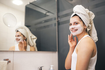 Young woman cleansing and scrubbing her face with cosmetics in the bathroom in front of a mirror, facial skincare routine