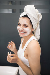 Young woman cleansing and scrubbing her face with cosmetics in the bathroom, facial skincare routine