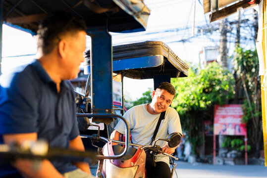 Two Southeast Asian tricycle drivers smile and enjoy a lighthearted conversation on the street, showing joy, friendship, and everyday camaraderie in their work.
