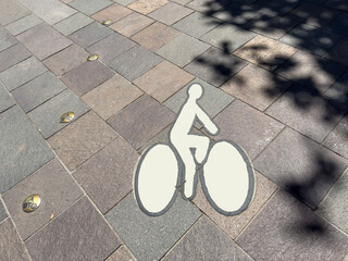 Urban Bicycle Lane Paving Sign on Textured Stone Sidewalk with Embedded Bronze Bike Markers