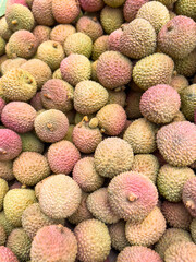 heap of  Fresh Lychee Fruits with Rough Pink-Green Skin in Natural Light on market.