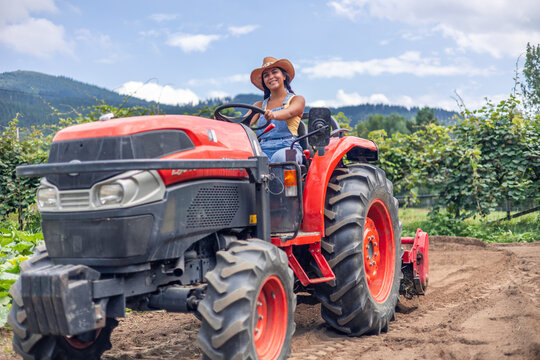 Latin farmer woman driving red tractor in cultivated field