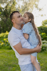 A father holds his daughter in his arms, and she gently kisses him on the cheek. The concept of family and the relationship between father and daughter.