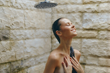 smiling woman enjoying outdoor shower with natural stone wall background, wet hair, peaceful...