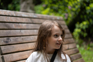 Young girl with a bright smile resting on a park bench. Concept: childhood happiness, peaceful...