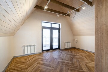 Bright attic room with herringbone wood floors. Double doors lead to a balcony. Light walls and a...