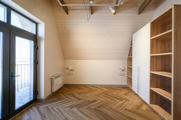 Bright room with herringbone floors, sloped ceiling, and large windows. A wardrobe stands against...