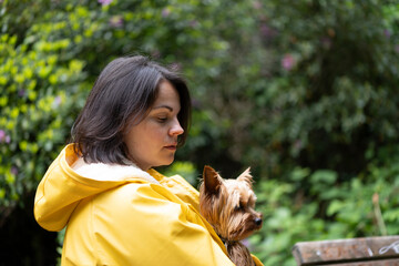Woman in bright raincoat with dog in arms in green forest. Concept: serene walk, mutual trust,...