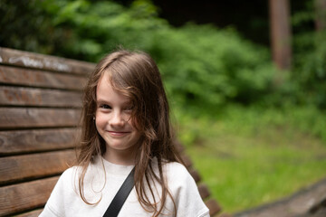 Little girl laughing on a wooden bench surrounded by greenery. Concept: natural joy, carefree...