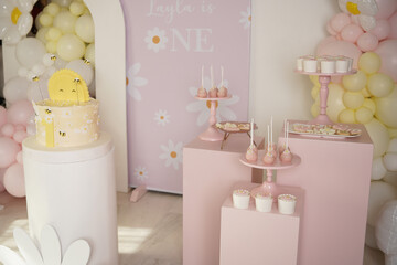 Adorable first birthday setup with a sun and bee-themed cake, pink daisy cake pops, and custom cookies. Surrounded by pastel balloons and floral decor—perfect for baby girl celebrations.