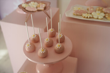 Elegant pink cake pops decorated with white fondant daisies, displayed on a soft pink...