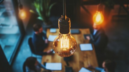 A glowing vintage filament light bulb hangs over a business meeting with blurred people and documents in the background.