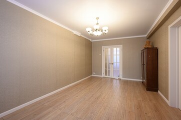 bright room features beige wallpaper, a light wood floor, and white trim. A chandelier illuminates...