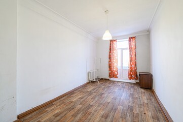 bright room with white walls and a wooden floor. A window with floral curtains lets in light....
