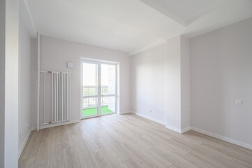 bright, empty room with wooden floors, white walls, a radiator, and a balcony door leading to a...