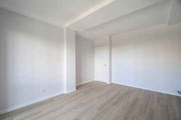 bright, empty room with light wood floors and white walls. A white door is visible in the back
