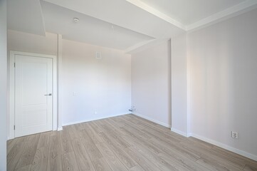 bright, empty room with light wood floors and white walls. A white door is visible in the back