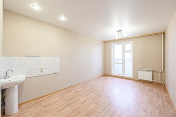An empty, bright room features a sink, laminate floor, and a window. The walls are beige, and the...