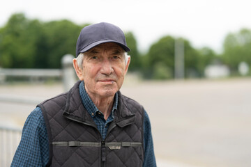 Smiling elderly man in baseball cap and vest standing outdoors in spring. Concept: active aging,...