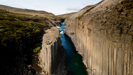 A stunning view of Studlagil Canyon showcasing towering basalt columns alongside a turquoise river,...