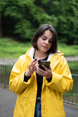 Portrait shot of woman in raincoat scrolling her phone in forest. Concept: modern lifestyle, contrast of technology and nature, quiet moment, outdoor habit.