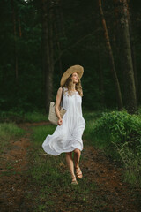 Young woman walking in forest wearing white dress and straw hat