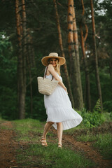 Smiling woman walking in forest wearing white dress and straw hat