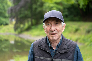 Elderly man in baseball cap and vest standing in spring forest, smiling. Concept: harmony with nature, peaceful aging, forest calm, seasonal renewal.