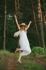 Happy woman dancing in forest wearing white dress and straw hat