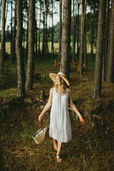 Young woman walking in forest wearing white dress and straw hat