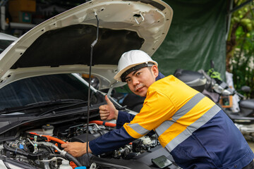 Mechanic in hard hat and safety jacket gives thumbs up while working on car engine