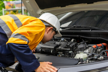 Mechanic in hard hat inspects car engine closely