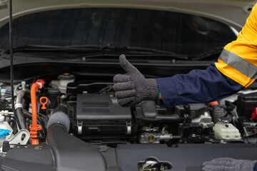Mechanic giving thumbs up near car engine, wearing gloves and uniform