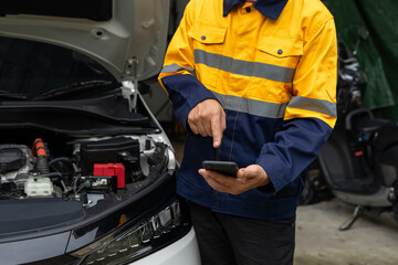 Mechanic using smartphone near car engine, wearing yellow and blue uniform