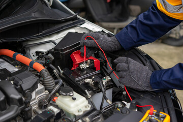 Mechanic testing car battery with multimeter in engine bay