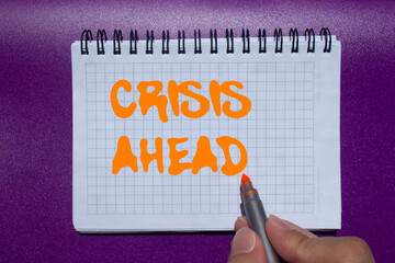 Crisis ahead message written on notebook page on purple background. Conceptual crisis ahead symbol....