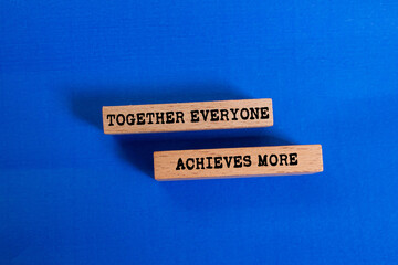 Together everyone achieves more message written on wooden blocks on blue background. Conceptual...