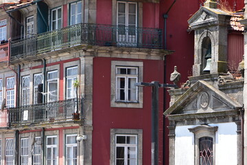 Small church with open belfry next to town apartment building with rows of balconies and French doors. Location: Porto Portugal