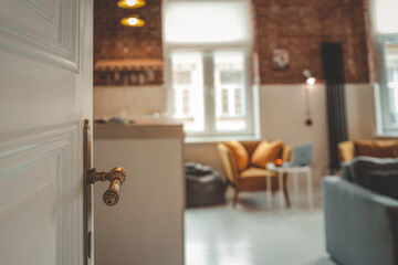Open white door with vintage brass handle leading into cozy loft interior with mustard armchairs,...
