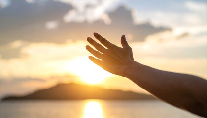 Silhouetted hand reaching towards golden sunset