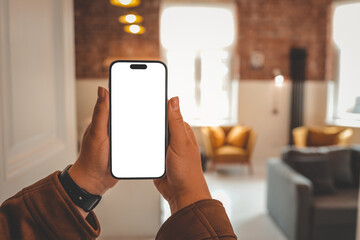 Person holding smartphone with blank screen in cozy loft interior with mustard armchairs, gray...