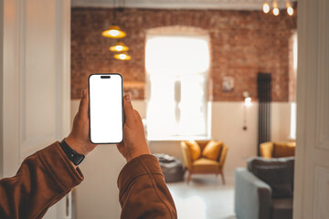 Person holding smartphone with blank screen in cozy loft interior with mustard armchairs, gray...