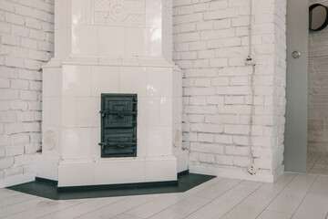 Vintage tiled stove in white interior with painted brick walls and wooden floor. Traditional...