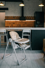 Modern baby high chair in stylish kitchen interior with bar stools, pendant lights, and patterned tiles. Cozy mix of industrial and homey design elements