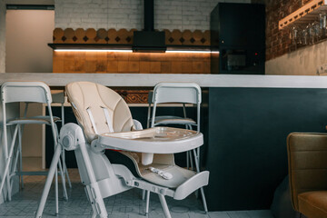 Modern baby high chair in stylish kitchen interior with bar stools, pendant lights, and patterned tiles. Cozy mix of industrial and homey design elements