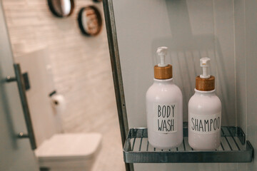 Minimalist bathroom shelf with labeled body wash and shampoo dispensers in white ceramic bottles...
