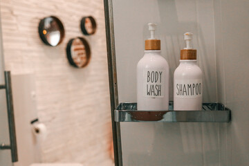 Minimalist bathroom shelf with labeled body wash and shampoo dispensers in white ceramic bottles...